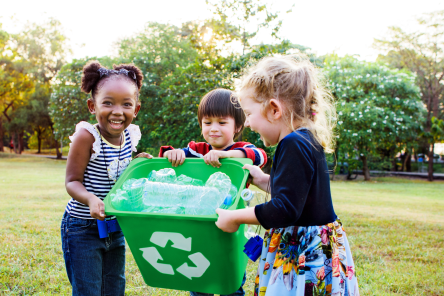School-aged children holding a green recycling bin